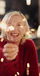 Christmas, face and woman in home, sparklers for celebration and happiness in living room. Apartment, smile and senior person in lounge, excited and funny with festive season, laugh and Xmas holiday