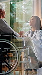 Doctor, old woman and holding hands with wheelchair in home for consultation, stroke or window in lounge. Medical professional, talk and senior patient with disability, support and rehabilitation