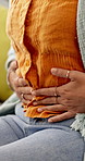Hands, stomach ache and rub on sofa in home with indigestion, cramps or constipation in living room. Woman, touch belly and pain with menstruation, inflammation and endometriosis on couch in house