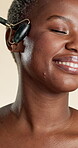 Jade roller, smile and skincare with black woman in studio for beauty, detox and glow treatment. Lymphatic drainage, facial tool and dermatology with person on white background for pamper and shine