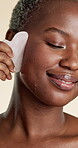 Gua sha, smile and skincare with black woman in studio for beauty, detox and glow treatment. Lymphatic drainage, facial tool and dermatology with person on white background for pamper and shine