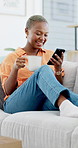 Black woman, coffee and laugh with phone on home sofa for funny post, blog update or online content. African person, drinking tea and relax on couch with technology, social media and reading on app