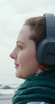 Happy woman, calm and headphones for music at beach, relax and listening to entertainment on weekend. Outdoor, tourist and person with technology for audio, smile and streaming song on winter holiday