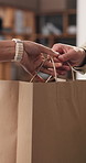 Shopping bag, gift and hands of people in home for sale, discount or promotion with purchase. Retail, giving and friends with commerce product for birthday present in living room at apartment.
