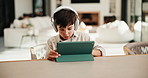 Tablet, headphones and kid in home for movie, series or show with subscription on app. Digital technology, relax and boy child streaming film online by table for internet entertainment in apartment.