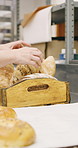 Person, hands and rolls with box in bakery for food production, catering service or distribution. Baker, pastry chef or packing bread with wooden crate for culinary art, inventory or stock in factory