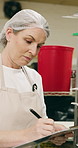 Woman, clipboard and check quality in bakery with inspection, manager or checklist at workplace. Mature person, industrial kitchen and writing on paper for safety and sanitation of baking process
