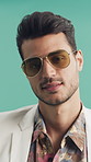 Face, fashion and shades with man in studio for summer aesthetic, apparel or holiday outfit. Clothing, confidence and sunglasses with person on green background for getaway, travel or vacation