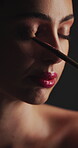 Cosmetics, eyeshadow or woman with brush in studio, apply powder or glamour aesthetic for glowing skin. Beauty product, facial routine and person with makeup for shine, tools and dark background