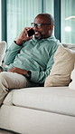Black man, phone call and relax on sofa with smile, chat and glasses with comfort in living room. Mature African person, happy and rest with mobile network, communication or laugh with story at house