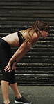 Runner, earphones and tired with woman in city for streaming service, health podcast and recovery. Wellness, exercise break and training music with person outdoor for stop, workout and radio