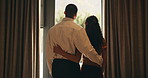Back, hug and love with homeowner couple at window together for relationship goals or success. Celebration, security and view with happy people in apartment for bond, mortgage or property investment