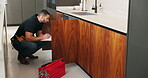Plumber, clipboard and writing in kitchen for inspection, maintenance service or repair project in home. Man, contractor or checklist at cupboard for problem solving, call out procedure or evaluation