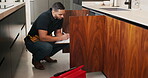 Plumber, clipboard and writing in kitchen for service, maintenance inspection or repair project in home. Man, contractor or checklist at cupboard for problem solving, call out procedure or evaluation