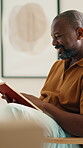 Reading book, relax and smile of black man on chair in home living room for literature hobby. Break, happy and story with mature person in apartment for fantasy or fiction novel on weekend morning