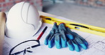 Construction, gloves or tools with helmet on table for development, layout or floor plan. Infrastructure documents, architecture or safety ppe, engineering drawing or building blueprint at empty site