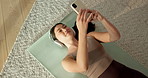 Woman, phone and headphones on yoga mat in home on floor with audio, post and relax for wellness. Asian person, sound and listen to music with exercise, subscription and above with streaming at house