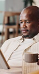 Home, coffee and man with tablet on break, online and watching movie with subscription or reflection. Black person, thinking and streaming film in living room, comfortable and relax with tea in house