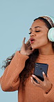 Woman, dancing and singing with headphones in studio for music, streaming and excited on blue background. Girl, person and listening to song, sound and audio subscription with happiness and funny