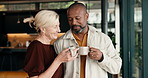 Coffee, cheers and mature couple in home with conversation, funny story or laugh for bonding together. Happy, interracial marriage and people in living room with joke, discussion or toast with drink.