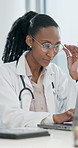 Doctor, glasses and typing on laptop in clinic for medical case review, treatment plan or admin. Professional, black woman or tech with eyewear for reading health database, research or insurance info