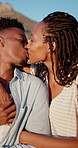 Hug, black couple and kiss on vacation at coast for anniversary getaway, bonding or weekend trip. Trust, love or happy people with affection outdoor for romantic holiday, relax or marriage connection