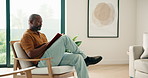 Relax, black man and reading book in home with peace, calm and literature on weekend break. Novel, study or mature person on armchair at living room with fiction story, information or knowledge hobby