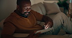 Black man, tablet and reading on sofa for social media, communication or entertainment in home. Mature person, smile and relax on living room couch with technology for online streaming or ebook