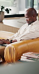 Happy, laptop and black man on sofa in home with reading ebook, blog or post on social media in living room. Calm, computer and African male person with online newsletter with typing in apartment.