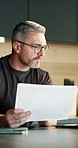 Remote work, paperwork and man with laptop in kitchen, risk assessment and research info on website. Freelancer, online and mature person with report, financial planning or investment review in house