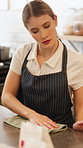Woman, inspection and cleaning in coffee shop with cloth, hygiene and maintenance for small business. Female person, wipe and polish counter in cafe for shine, work protocol and customer service.