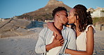 Hug, black couple and kiss on vacation at beach for anniversary getaway, bonding or weekend trip. Trust, love or happy people with affection on sand for romantic holiday, relax or marriage connection