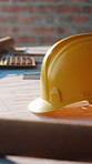 Construction, helmet and sunlight with floor plan on desk at building site for property development. Blueprint, hardhat and safety with documents on table for architecture or project management