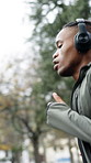 Exercise, man or running with headphones in rain for fitness dedication, pace training or playlist. Active, black person or winter workout at park with music, endurance challenge or health discipline