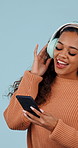 Woman, dancing and singing with headphones in studio for music, streaming and excited on blue background. Girl, person and listening to song, sound and audio subscription for groove and wellness