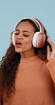 Woman, dancing and energy with headphones in studio for music, streaming and excited on blue background. Girl, person and listening to song, sound and audio subscription for moving body with smile