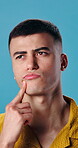 Confused, man and thinking in studio, curious and plan for choice with frown or uncertain expression. Blue background, unsure and person with questions, reflection and contemplating decision and idea