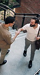 Happy, people and fist bump in office with greeting, conversation or morning motivation for coworker. Above, men walk or arrival in creative company with stairs, respect or encouragement to start day