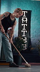 Sweeping, cleaning and man in tattoo parlor for maintenance, chores and responsibility in store. Creative, small business and person with broom for dust, hygiene and mess in shop for ink service
