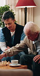 Caregiver, playing and old man at house with chess, strategy and competition with cognitive games. Nurse, piece and senior person on sofa for challenge, contest tactics and skills for match checkmate