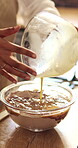 Home, hands and baking mixture in bowl for cake batter, preparation process and culinary skills. Baker, person and pour raw ingredients in kitchen for handmade dessert, muffin snack and weekend hobby