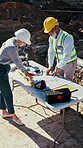 Architect, blueprint and people outdoor at construction site with discussion, building and excavation. Contractor, man and woman by floor plan for teamwork, collaboration or civil engineering project