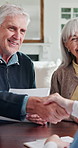 Document, elderly couple and handshake with financial advisor, agreement or smile in home. Retirement, man or woman shaking hands with paper for legal contract, deal or happy with pension application
