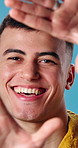 Face, frame or studio with happy man for selfie, camera angle or capture moment on a blue background. Portrait, male person or smile with hands or cover for photography, picture or social media post