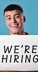 Hiring, poster and face of man in studio for recruitment, advertising and marketing of job. Happy, portrait and hr manager with sign for work opportunity, onboarding or offer by blue background.