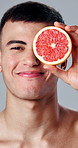 Skincare, grapefruit and face of man in studio for beauty, health and natural cosmetic routine. Happy, nutrition and portrait of person with citrus fruit for dermatology treatment by white background