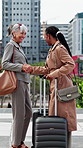 Business, women and city with handshake for introduction, meeting or commute together. Female people, employees or colleagues shaking hands with smile, luggage or suitcase for work trip or travel