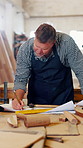 Carpenter, writing and notes with man in workshop for manufacturing or production process. Creative, design and drawing with mature person in woodworking studio for project, planning and research