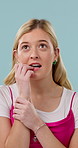 Biting nails, face and nervous with woman in studio for anxiety, concern or thinking. Chewing fingers, stress and worry with person on blue background for contemplation, coping mechanism or mistake