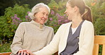 Talking, caregiver and old woman on bench in garden for bonding, support and conversation outdoor. Retirement, happy and nurse with elderly person for wellness, care and fresh air for assisted living